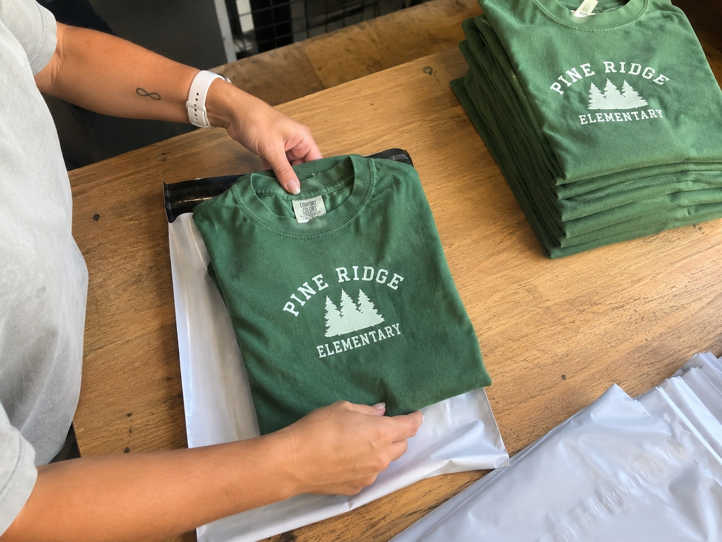 A folded custom-printed school t-shirt being packed into a shipping mailer