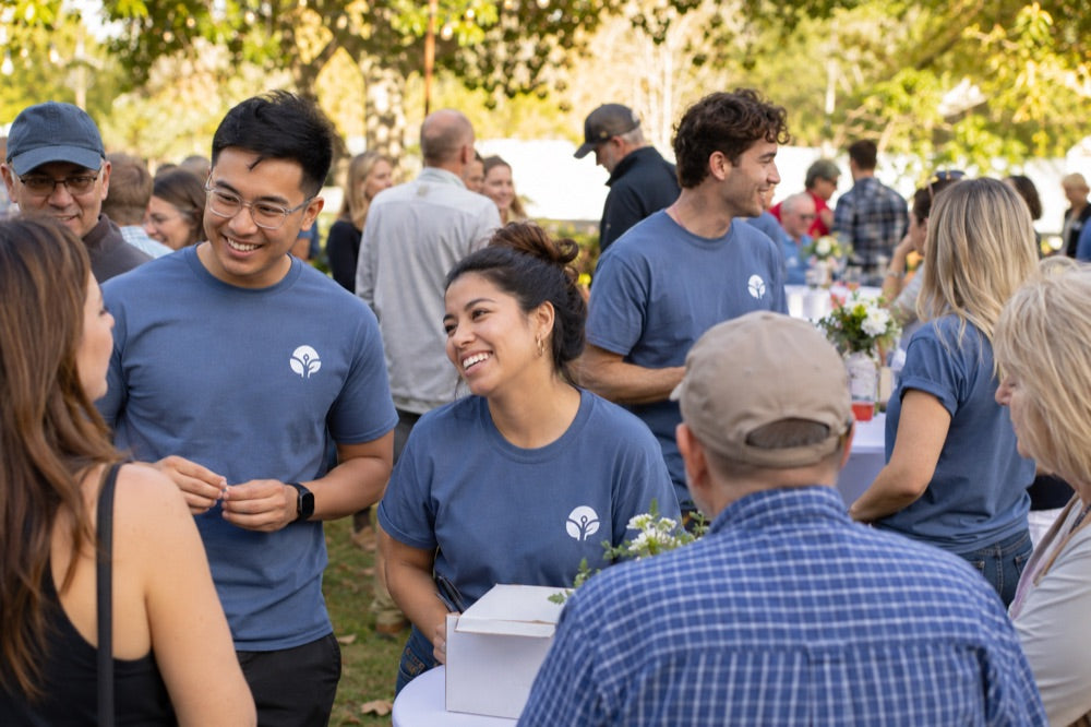 Volunteers in matching blue logo t-shirts talking with guests at an outdoor fundraiser