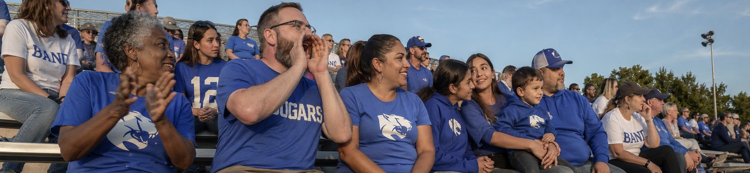 Multi-generational families cheering in the stands in custom school fan tees and band shirts