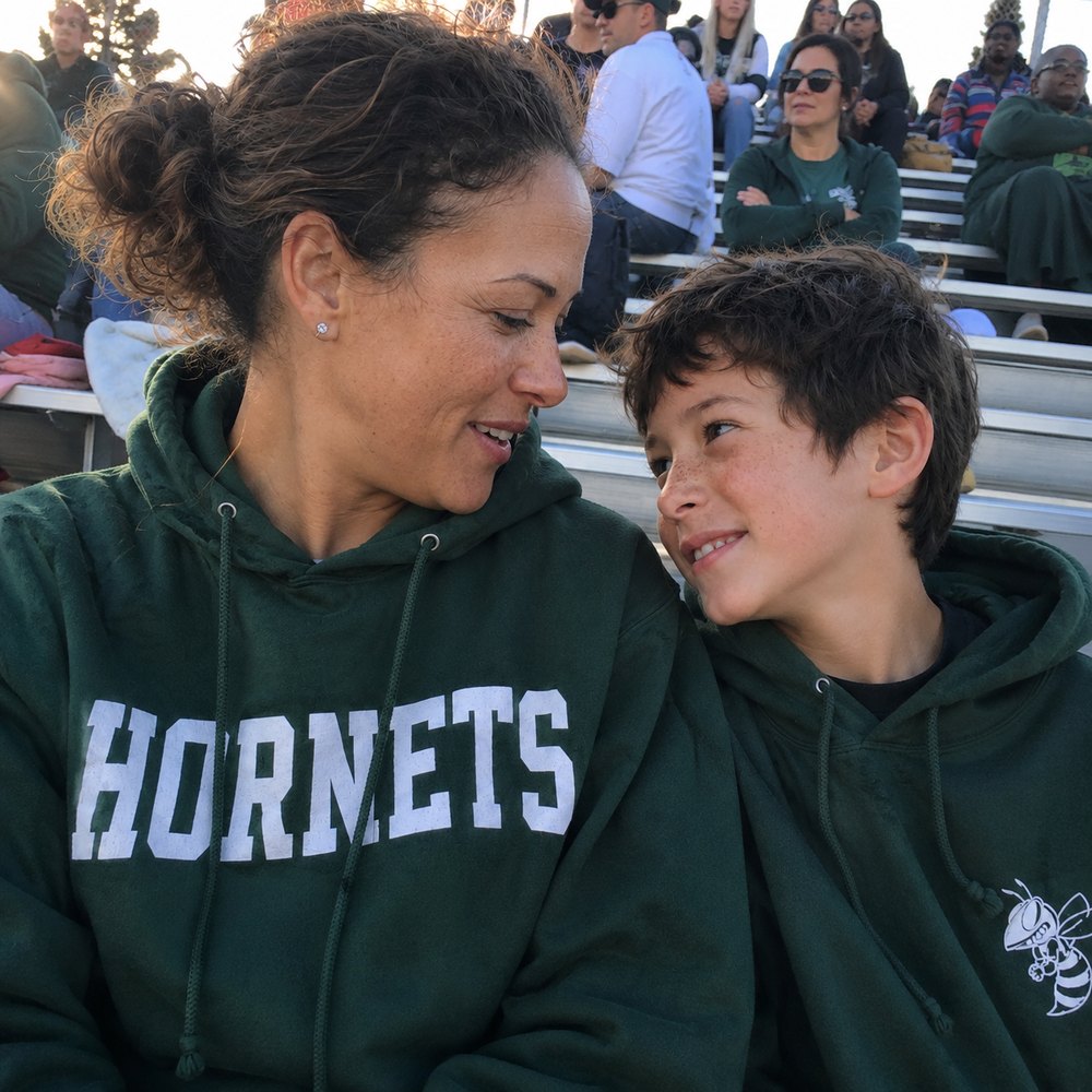 A mom and her son laughing together in matching school spirit hoodies